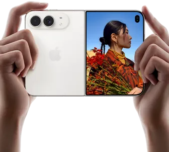 iPhone Duo, Star White colour, held by two hands in horizontal orientation, unfolded, left panel shows 48MP Dual Fusion rear cameras, right panel shows person getting their picture taken on outer display, the subject of the photo is able to see their face as their picture is getting taken using Duo Preview