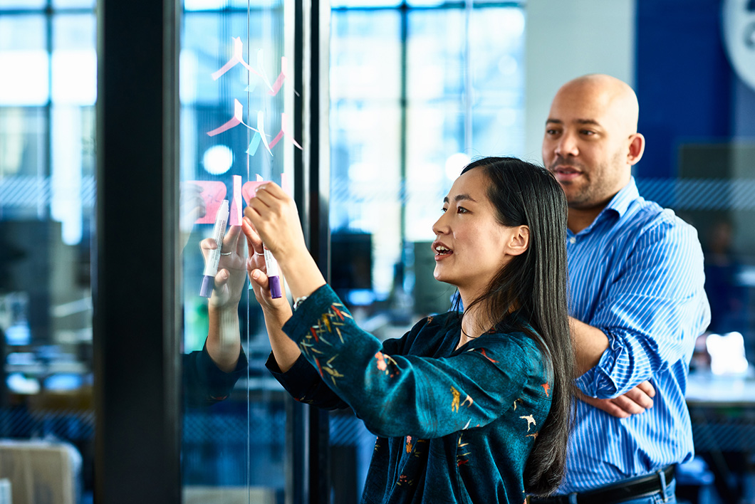 Candid portrait of attractive businesswoman brainstorming with colleague, using adhesive notes for planning and strategy